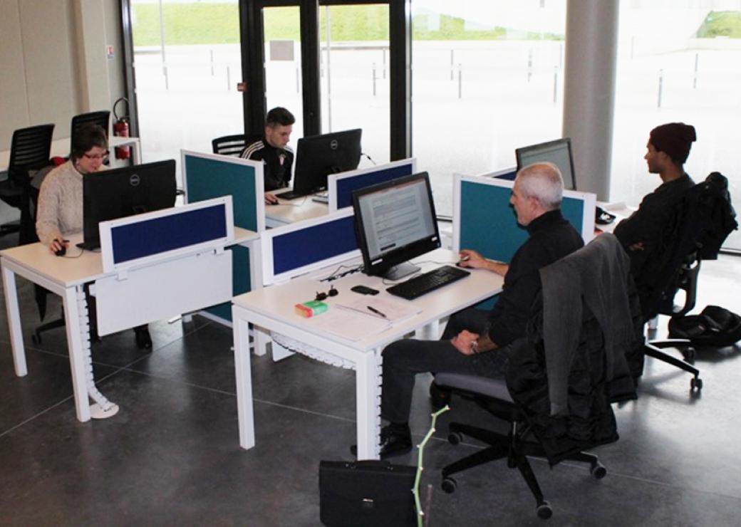 Dans une salle informatique, quatre personnes sont face à des ordinateurs