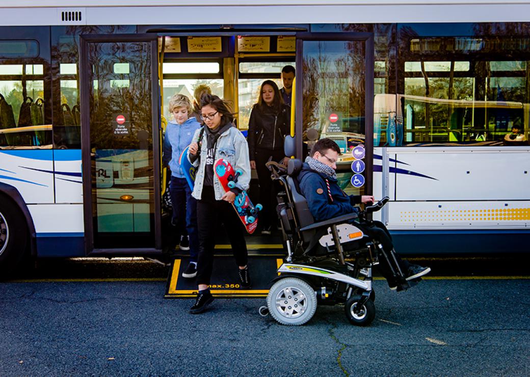 Photo d'un bus d'où descendent des personnes, dont un jeune homme en fauteuil roulant