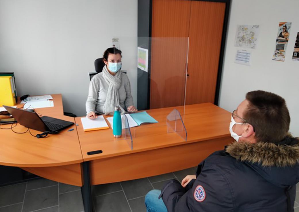 Une jeune femme assise derrière un bureau fait face à un homme assis de l'autre côté du bureau.