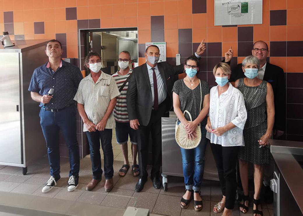 Devant un mur carrelé et entouré de mobilier en inox, des hommes et des femmes posent pour la photo. Ils portent un masque chirurgical.