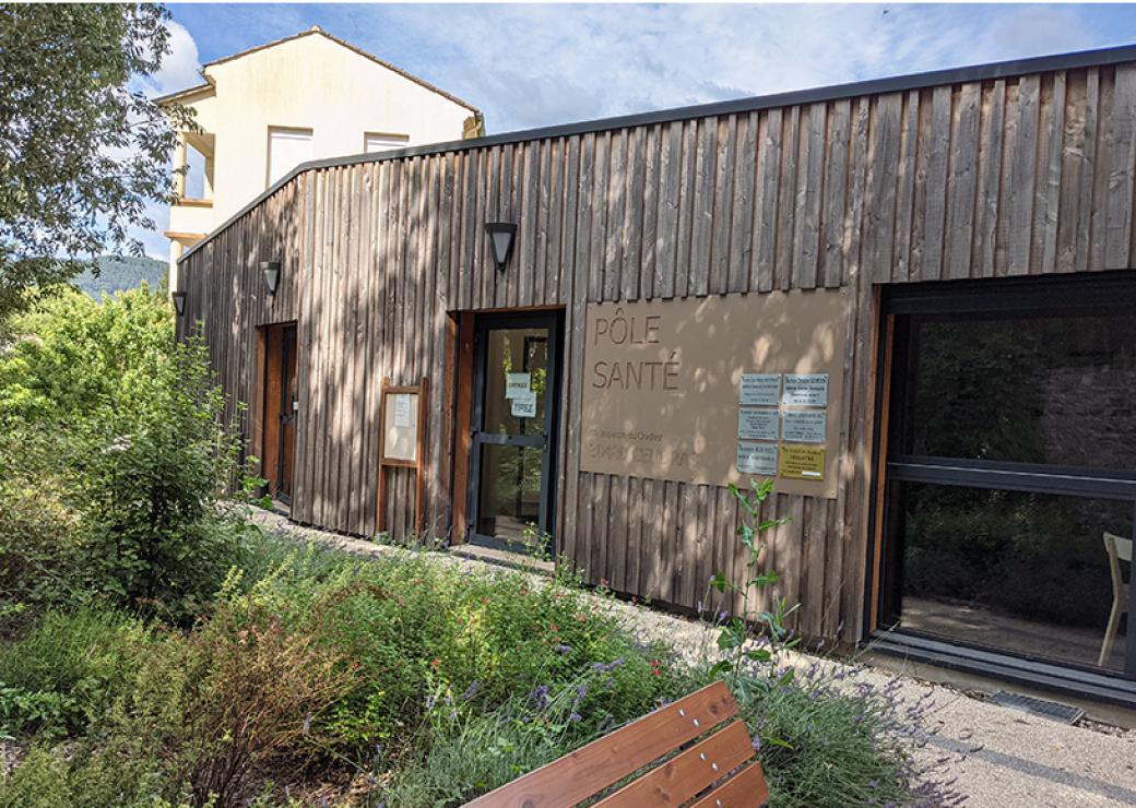 Photo d'un bâtiment de plain pied, dont la façade est couverte de bois. Un panneau indique "pole santé"