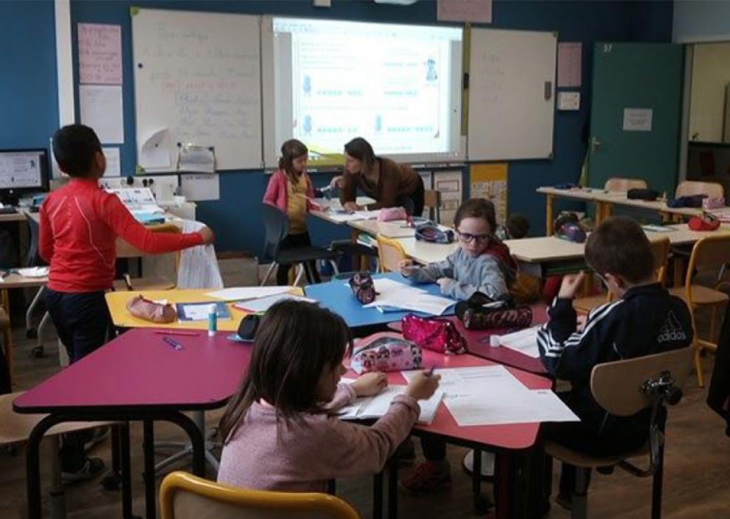 La photo montre une classe où les tables sont installées en étoile, avec des enfants en mouvement