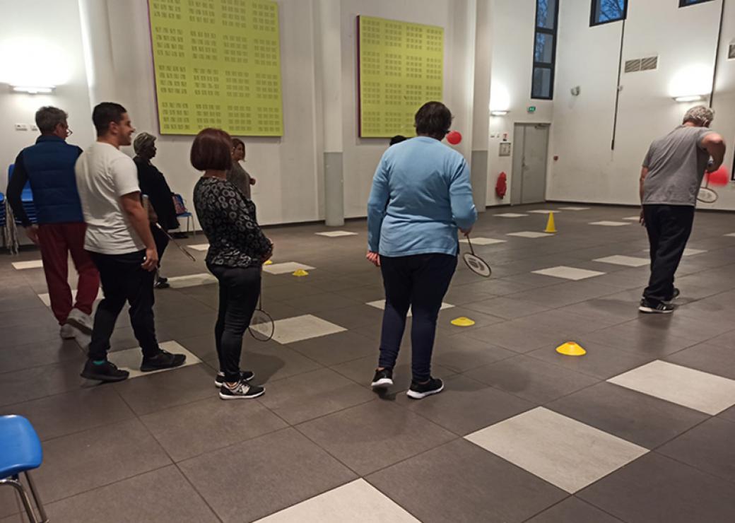 Huit personnes de dos dans une grande salle tiennent à la main une raquette de badminton