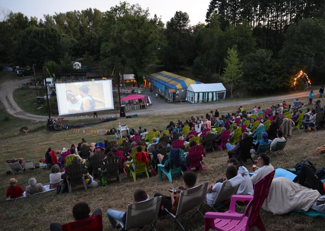 Sur une pente, des fauteuils colorés sont installés, occupés par des personnes qui regardent un film sur l'écran en contrebas