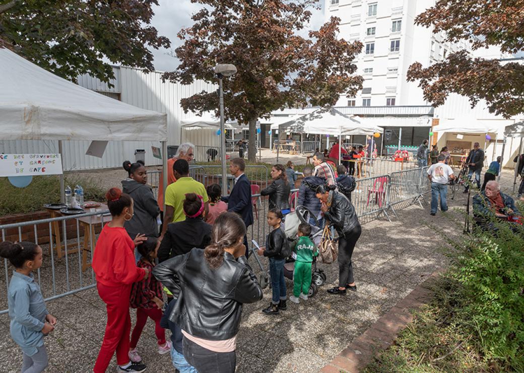 Des enfants et des familles attendent auprès d'un stand de kermesse, sur un parvis entouré d'immeubles