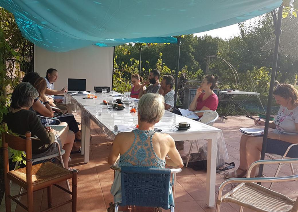 Protégés du soleil par un tissu bleu, une dizaine de personnes sont réunis autour d'une table dans un jardin