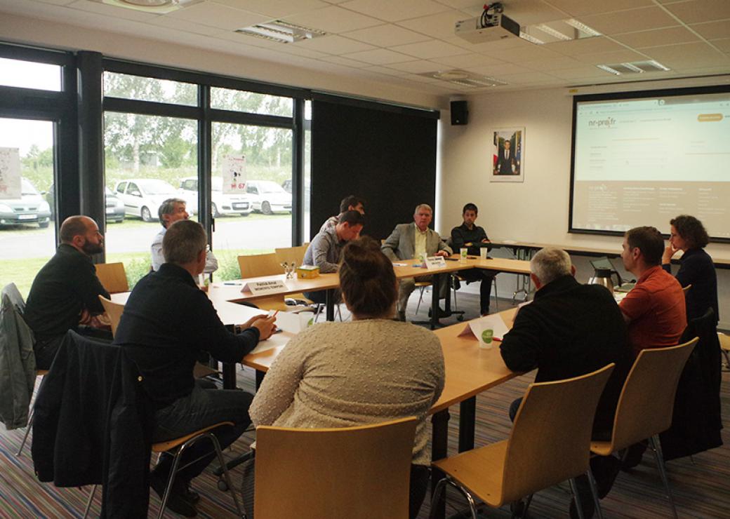 Dans une salle de réunion, une dizaine de personnes sont assises autour d'une grande table