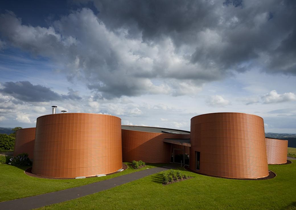 Sous un ciel chargé de nuages, un bâtiment composé de plusieurs tubes, de la couleur de la terre cuite