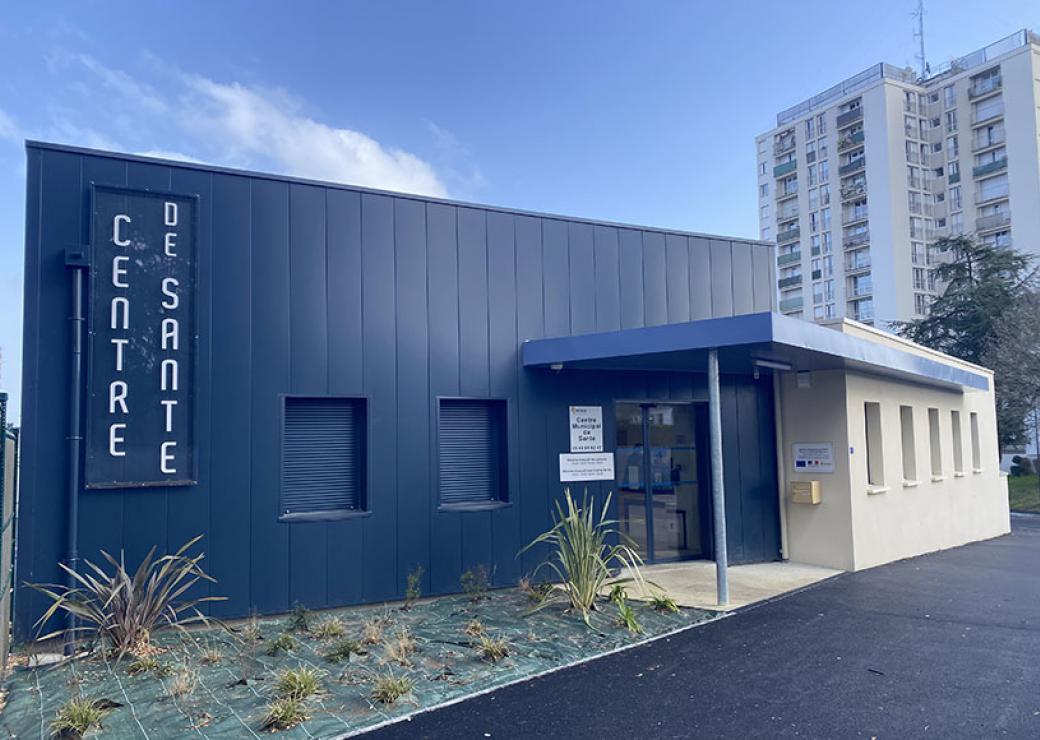 Photo d'un bâtiment moderne sur lequel on peut lire "Centre de santé". En arrière plan, une tour d'habitation