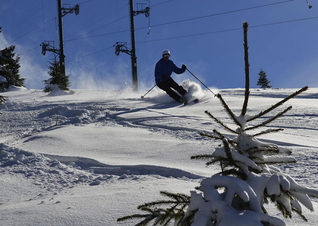 Plan large d'un skieur évoluant sur une pente enneigée, avec des pilônes en fond