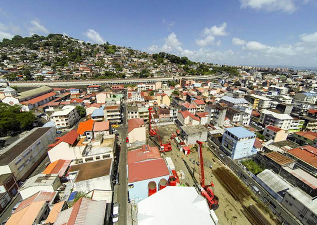 Vue aérienne d'un chantier avec deux grues rouges, sur une parcelle au milieu d'une ville