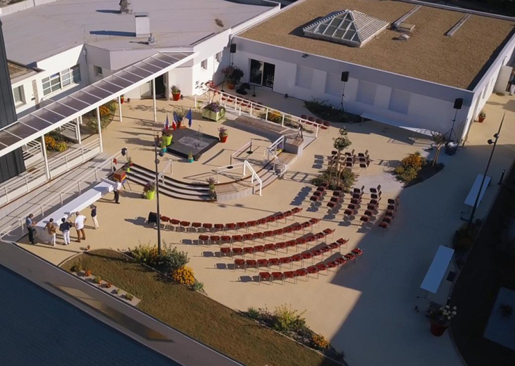 Vue aérienne d'une place où sont installées des chaises orientées vers un podium entouré de drapeaux