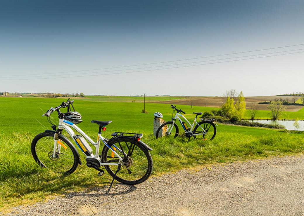 Sur un chemin de campagne, deux vélo blancs sont posés sur la béquille. Ciel bleu et herbe verte.