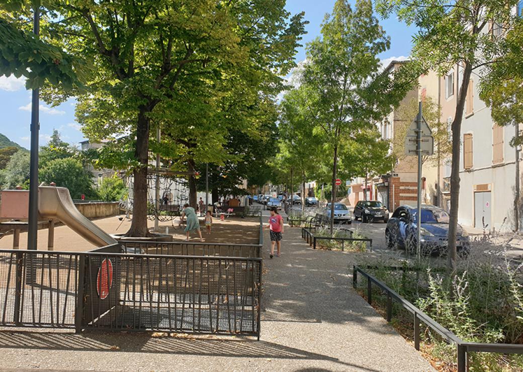 Photo d'une aire de jeux pour enfants, ombrée de platanes et bordée de bâtiments anciens