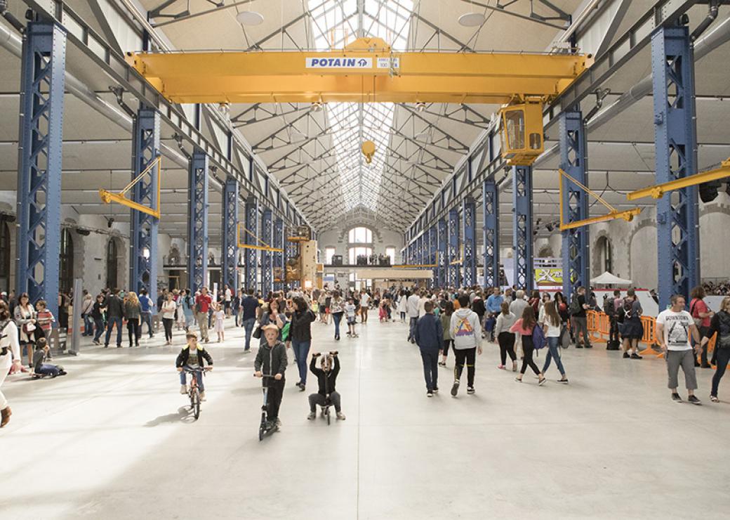 Une très grande halle au toit soutenu par des piliers d'acier. Des personnes déambulent