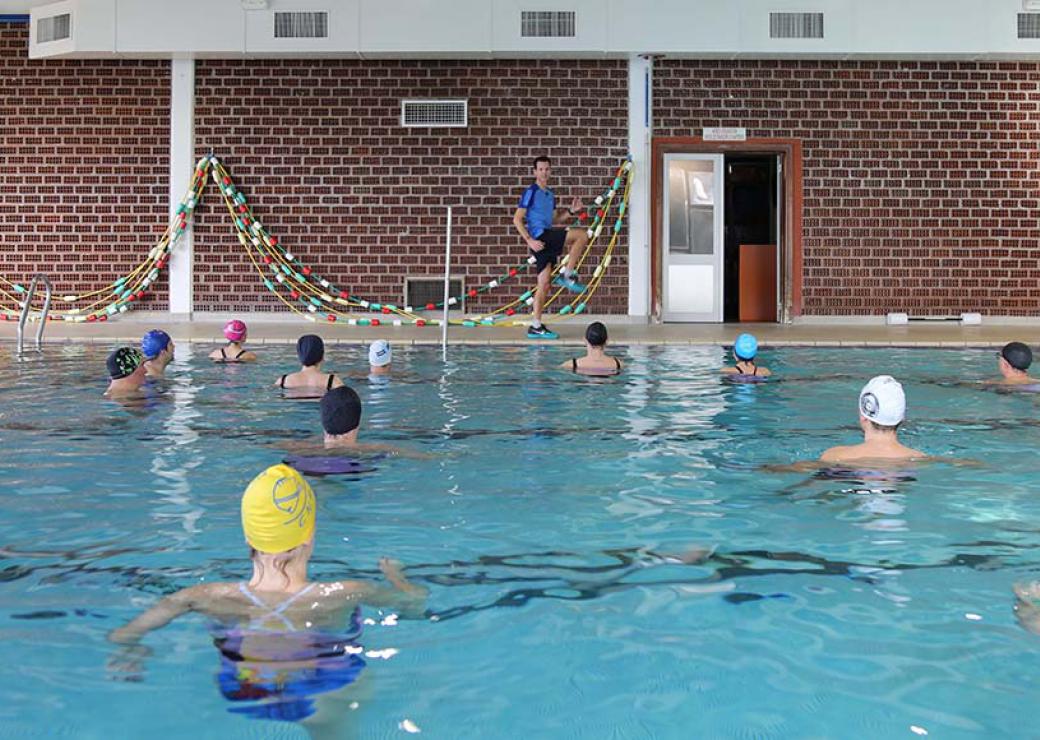 Dans une piscine, un homme montre des mouvements à des personnes immergées et coiffées d'un bonnet de bain
