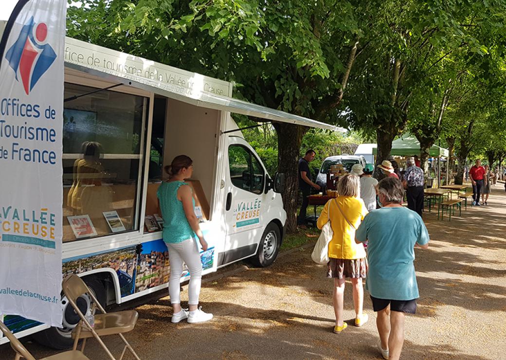 Sur un marché, un camion dont le côté est ouvert en comptoir. Sur un kakemono posé à côté, on peut lire Offices de tourisme de France vallée de la creuse