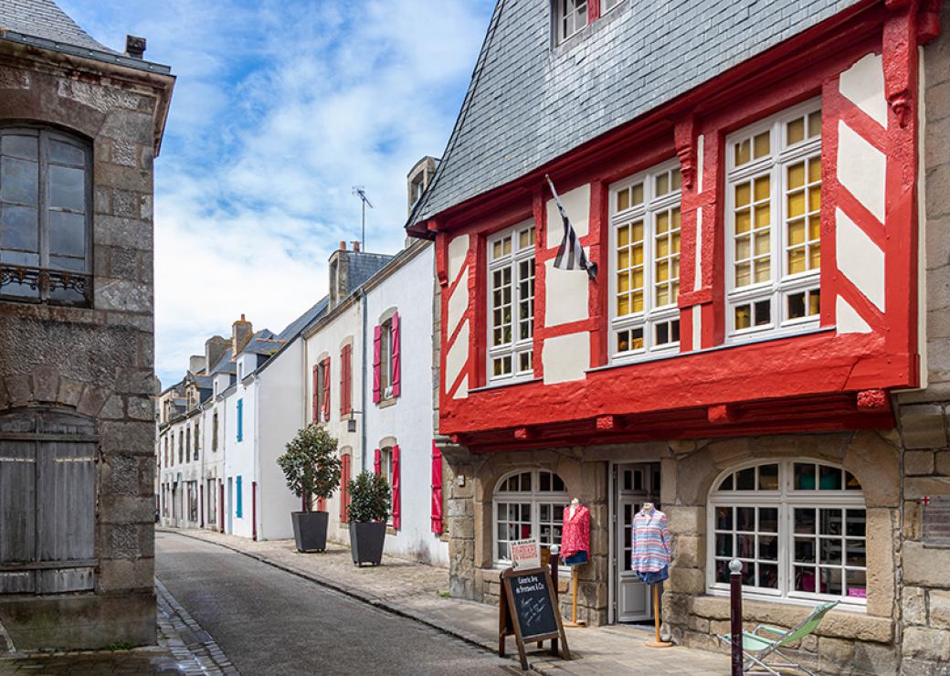 Par beau temps, une rue dont le première maison est une maison à colombages dont les bois sont rouges