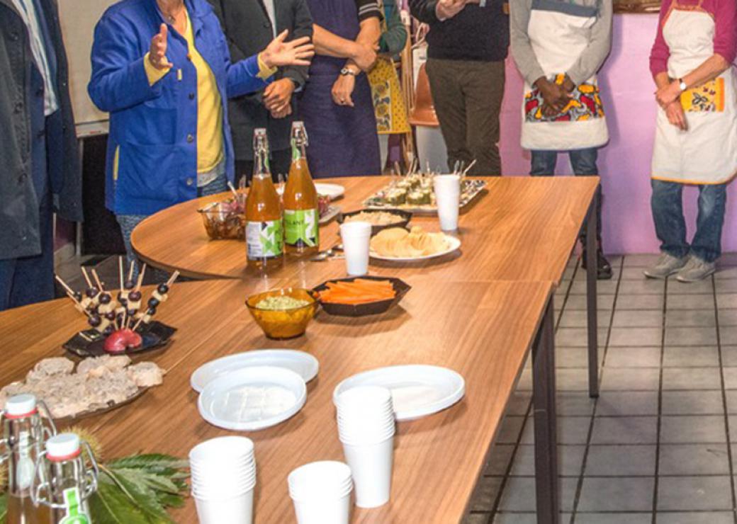 Sur une table, des mets sont disposés. Des personnes sont en cercle autour ce cette table.