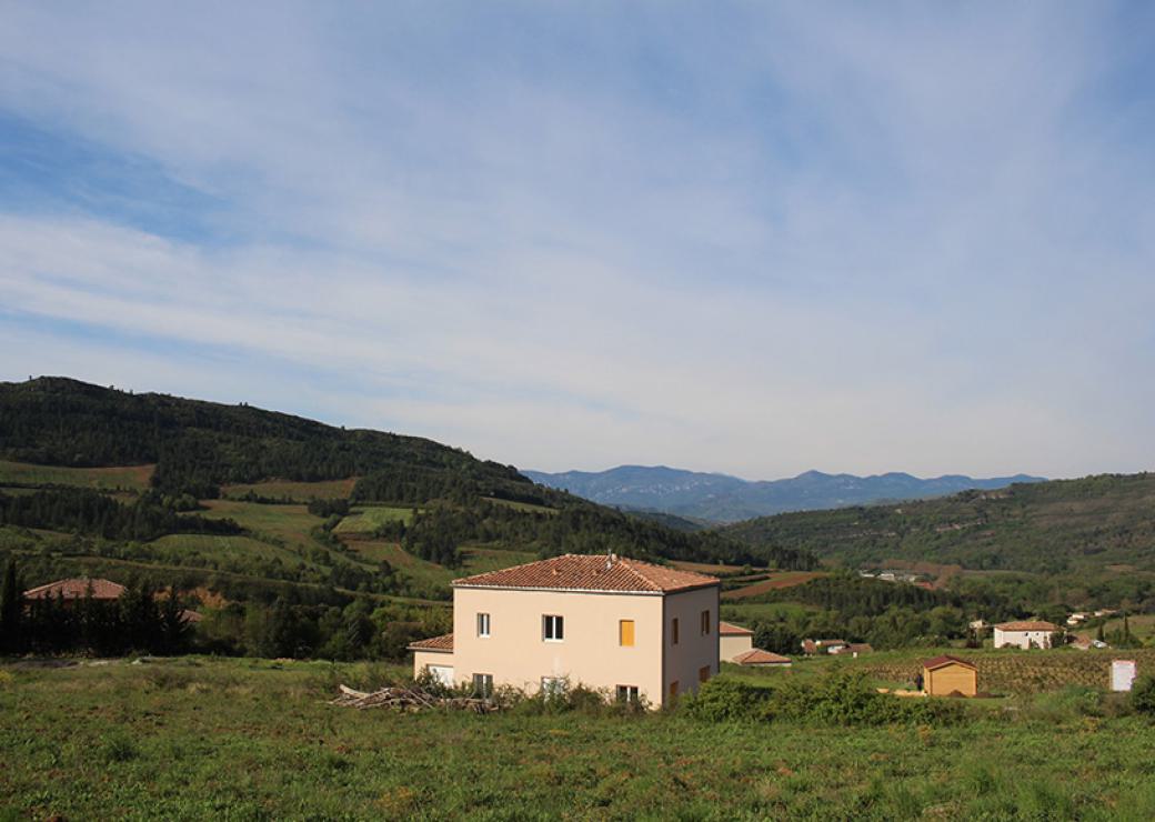 Dans un paysage de collines verdoyantes, une maison neuve construite dans la pente, entourée d'un chapelet de six autres maisons neuves