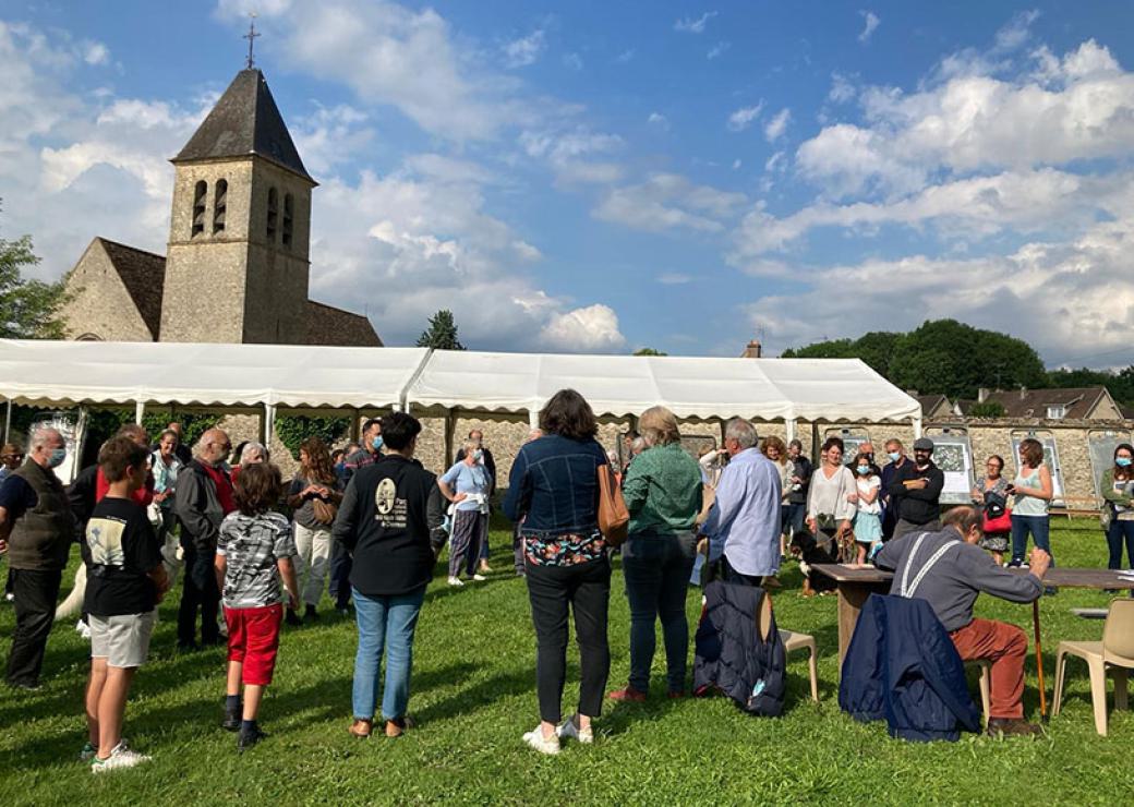 une cinquantaine de personnes se tient debout sur une pelouse. En fond, le clocher d'une église