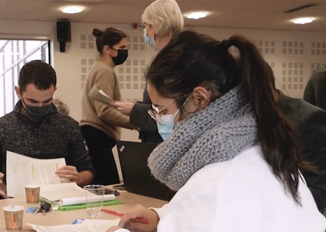 Des personnes portant un masque chirurgical sont assises à des tables et analysent des documents