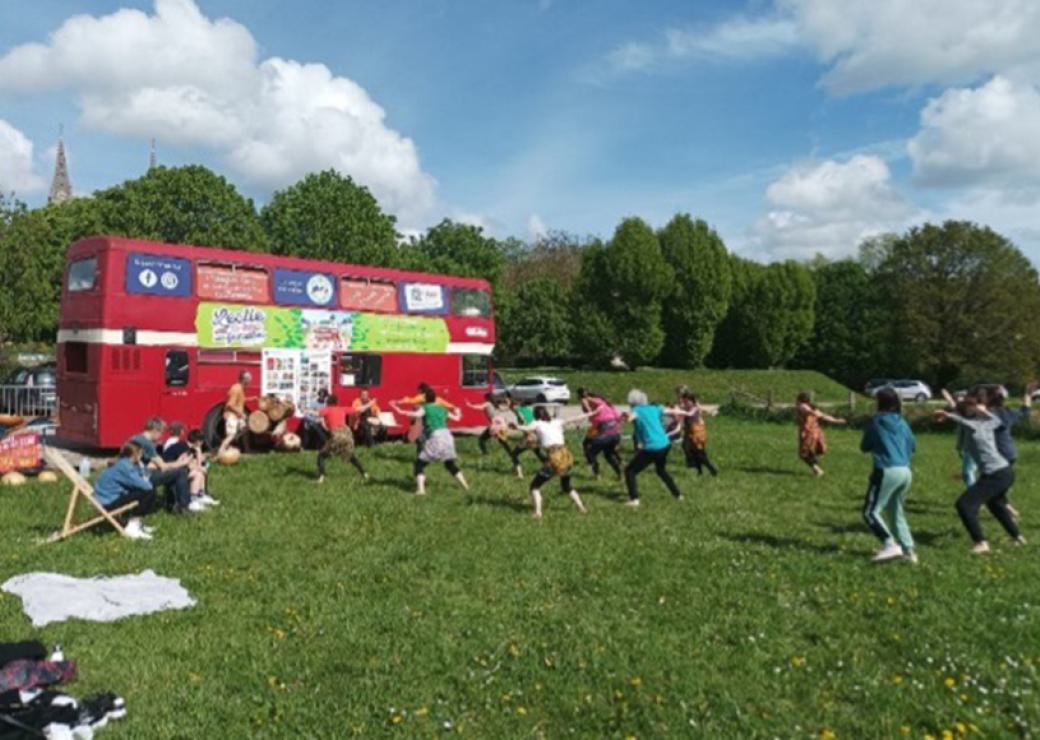 Des personnes font du sport sur une pelouse, en face d'un bus anglais rouge