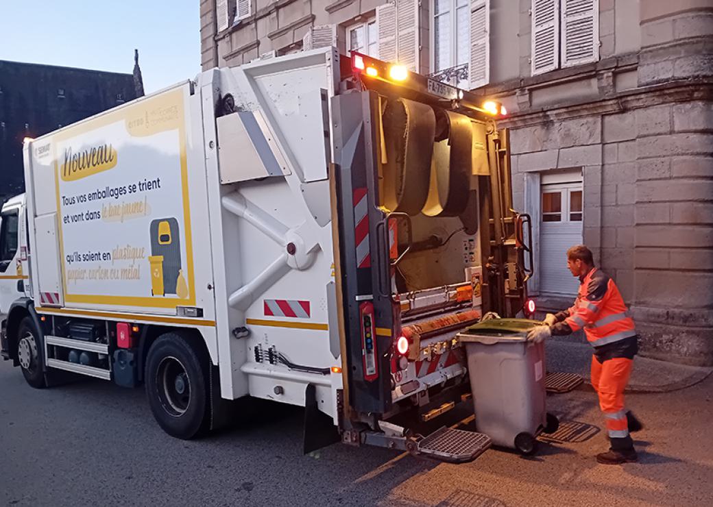 Une homme habillé en vêtements orange pousse une poubelle vers un camion benne