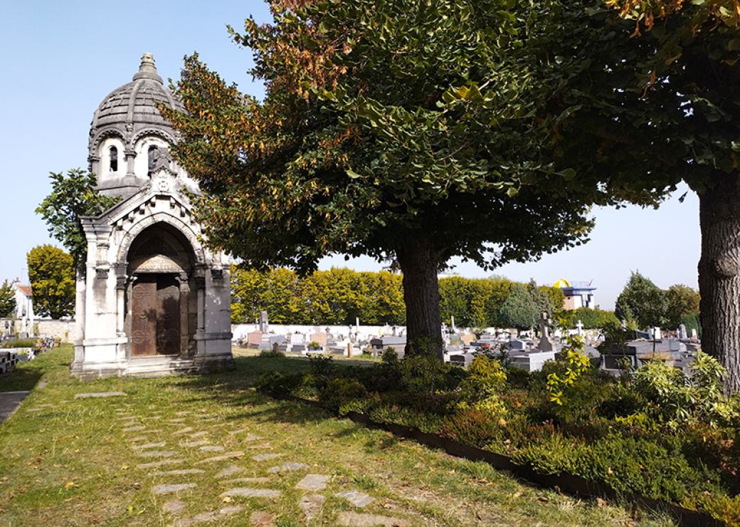 Dans un cimetière, une allée de gazon, pavée de larges dalles mène à un mausolée