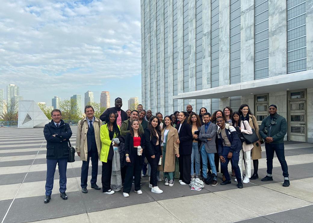 Sur le parvis d'un building, avec des gratte ciels en arrière plan, une vingtaine de jeunes posent pour la photo