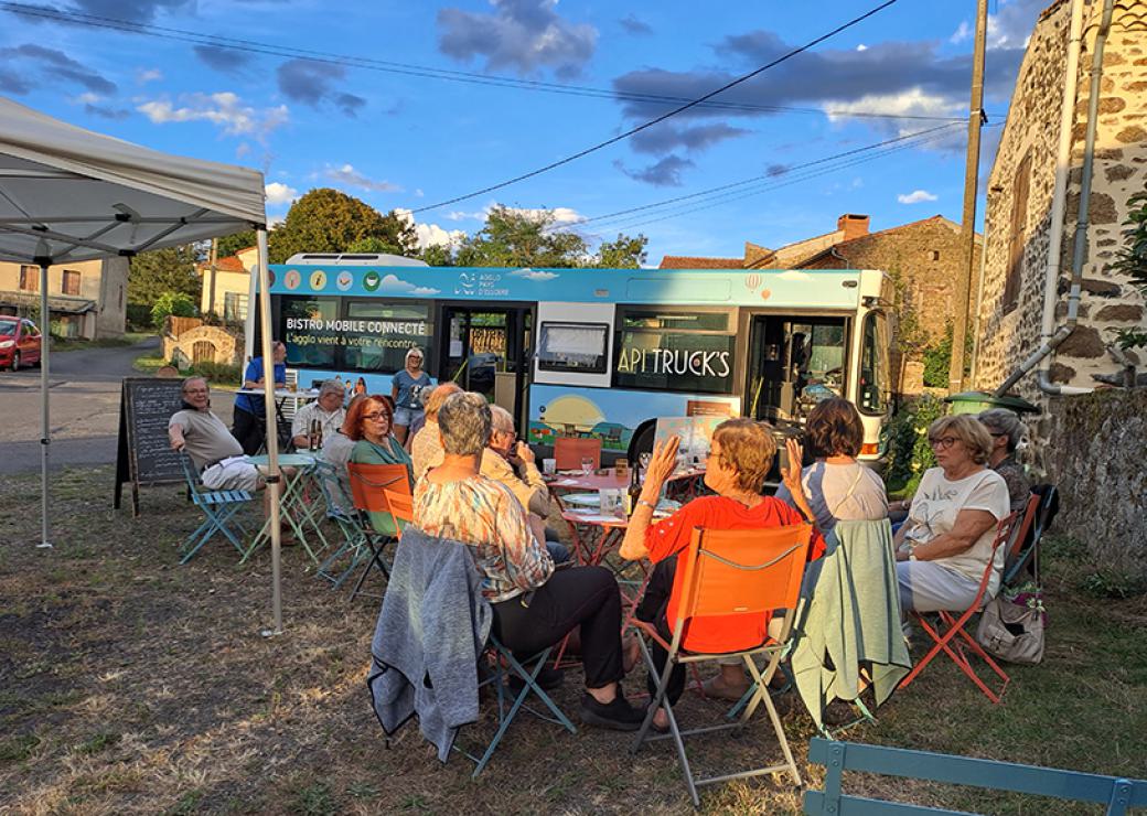 Une dizaine de personnes sont attablées à une terrasse installée devant un bus 