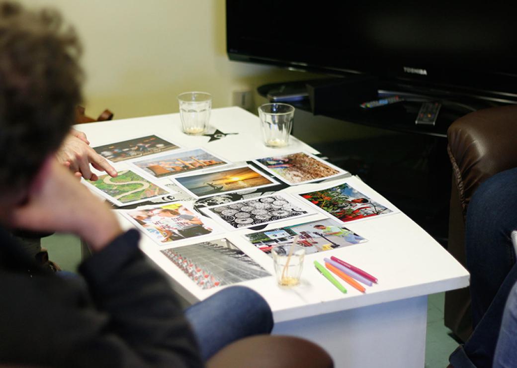 Sur une table basse, des images sont posées, ainsi que des verres. On devine des personnes autour de la table