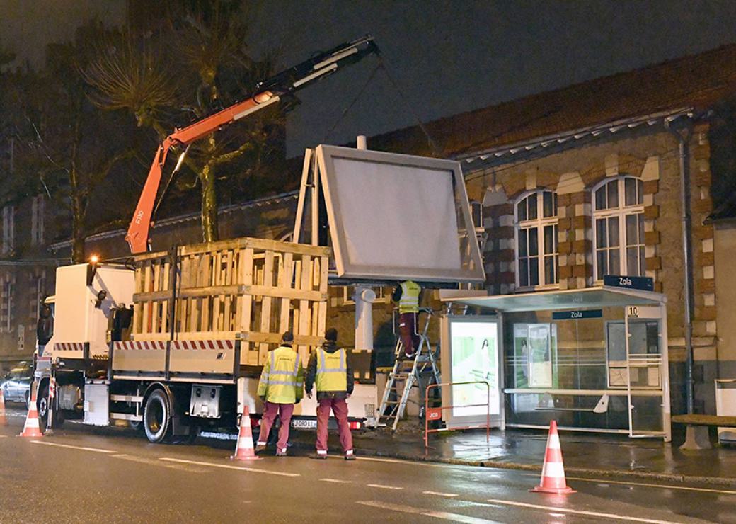 De nuit, un camion-grue démonte la structure d'un très grand panneau d'affichage