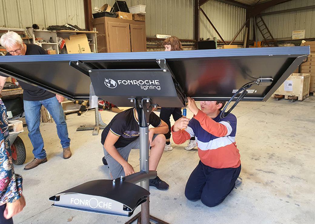 Dans un hangar, des personnes sont agenouillés et intervienne sur le pied d'un panneau solaire