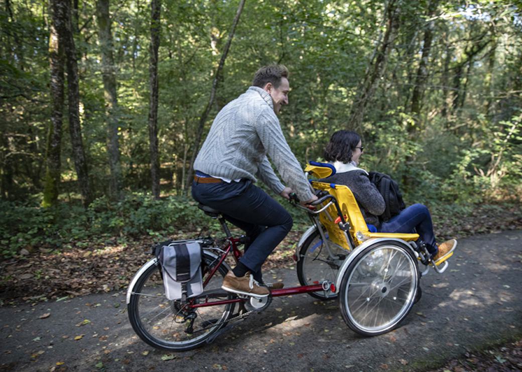 Une personne pédale sur un vélo. À l'avant du vélo, une autre personne et assise, qui ne pédale pas