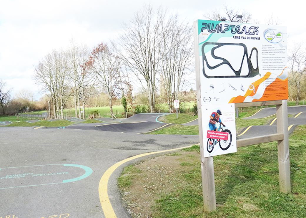 Vue d'une piste goudronnée et bosselée, avec un panneau indiquant "pumptrack"