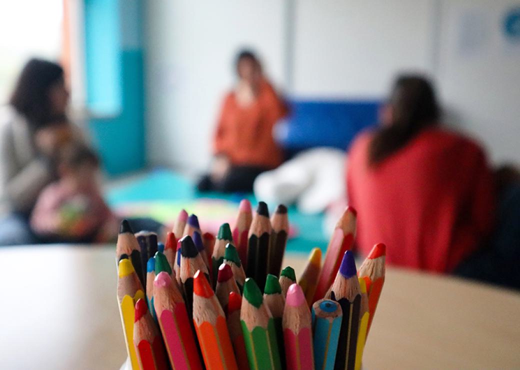 Un pot de crayons de couleurs au premier plan et au deuxième plan, flous, trois silhouettes d'adultes et une silhouette d'enfant