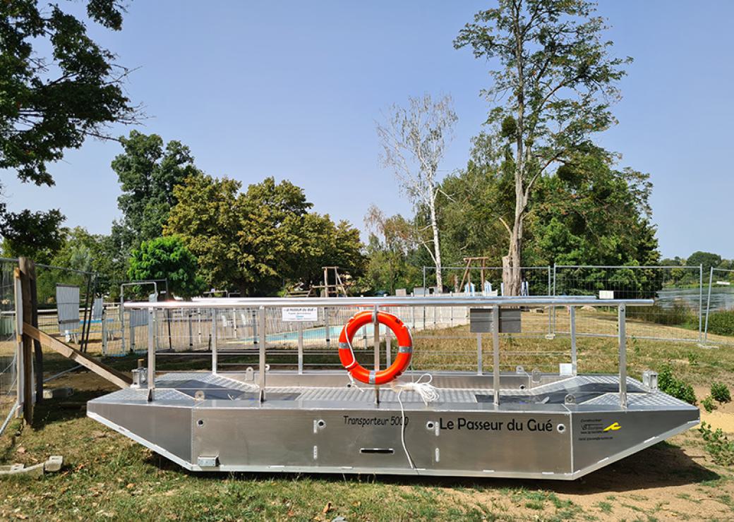 Une barge métallique à fond plat est posée sur la berge d'un cours d'eau