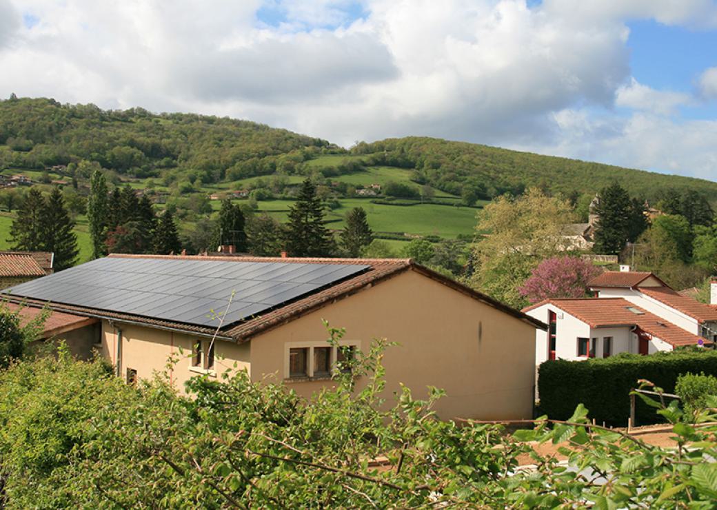 Vue aérienne d'un hangar dont le toit est couvert de panneaux solaire. Autour, paysage vert.