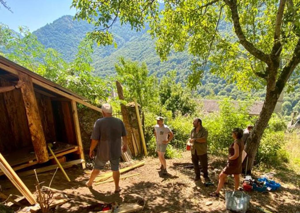 Quatre personnes se tiennent aux abords d'une construction de bois, dans un paysage de collines boisées