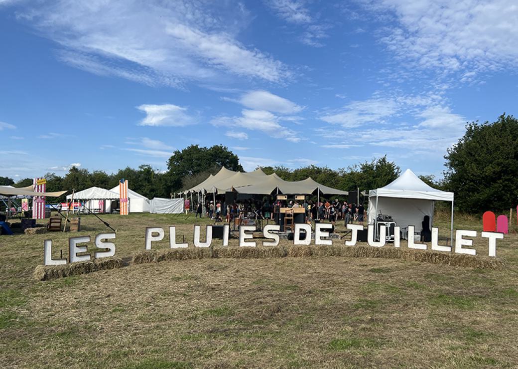 Champ hérissé de tentes. Au premier plan, des lettres posées sur le sol, on peut lire "les pluies de juillet"