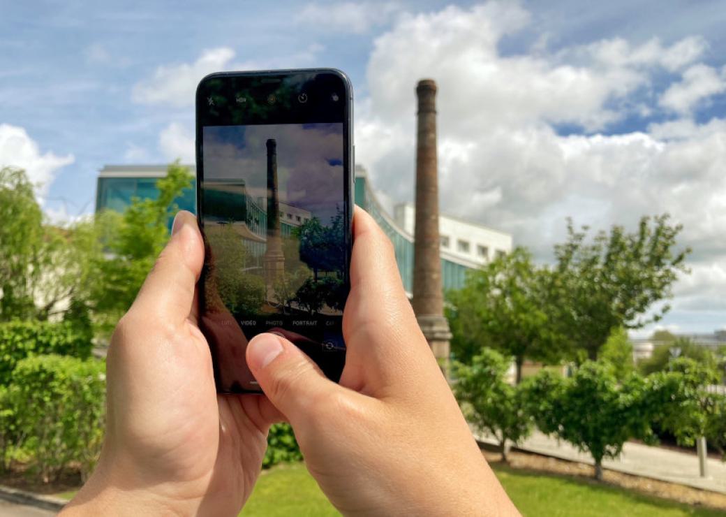 Un smartphone dans les mains d'une personne qui prend en photo une haute cheminée en briques