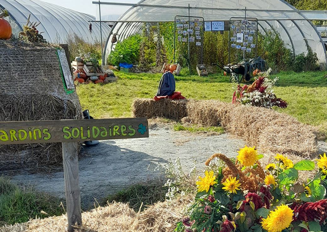 Des bottes de paille, des serres et un panneau "jardins solidaires"