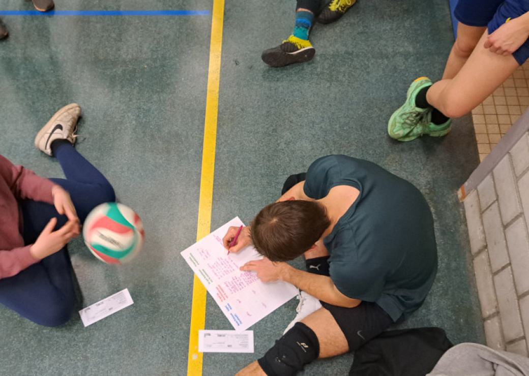 Une personne assise sur le sol rempli un formulaire, vu d'en haut, avec un ballon de volley ball lancé vers la personne 