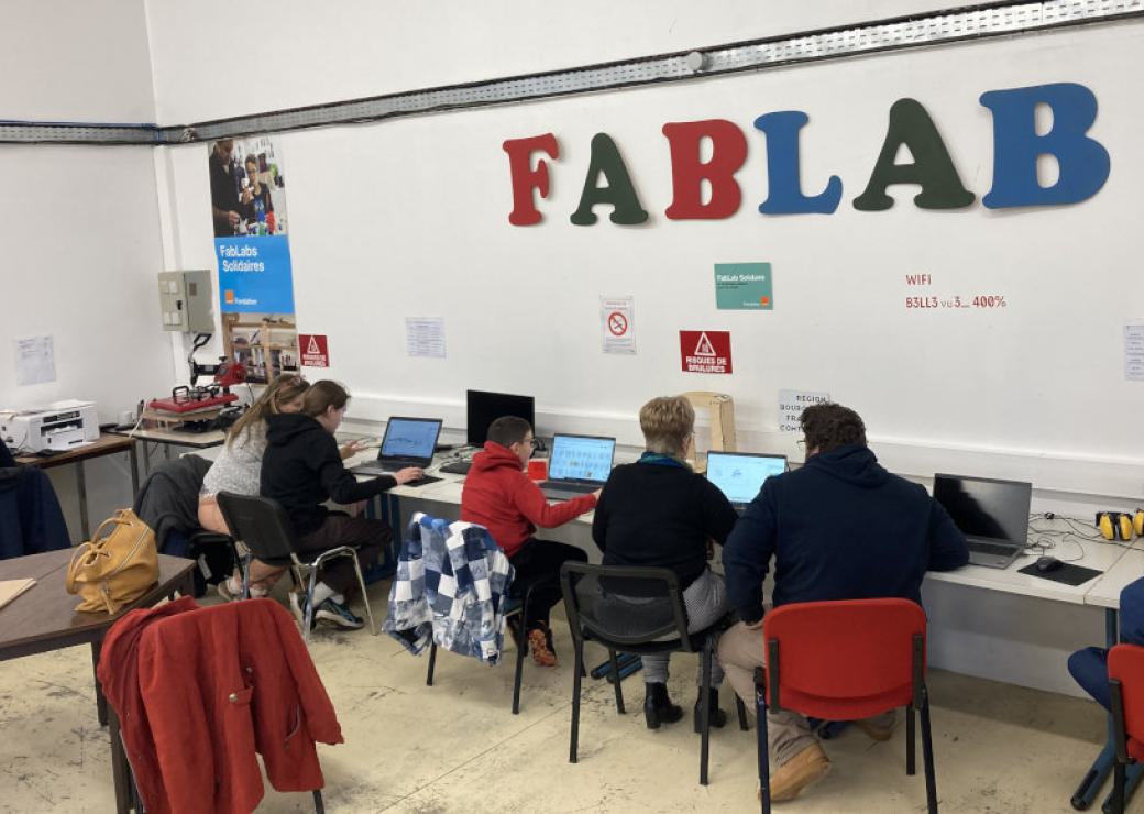 Des enfants sont devant des ordinateurs. Sur le mur au dessus d'eux, on peut lire "Fablab"