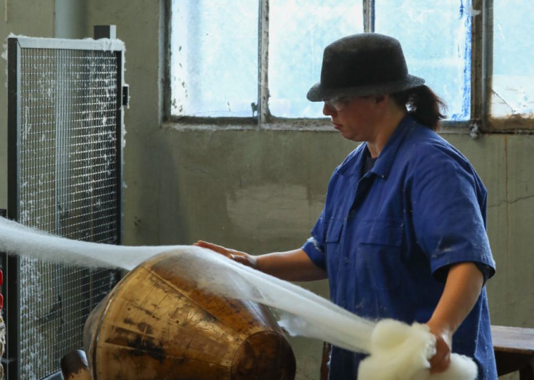 Une personne coiffée d'un chapeau tient un voile de textile qu'elle appose sur un tour de bois