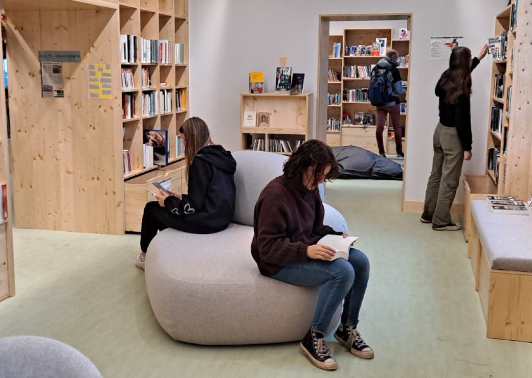 Des personnes sont assises et lisent sur un pouf, entourés d'étagères remplies de livres