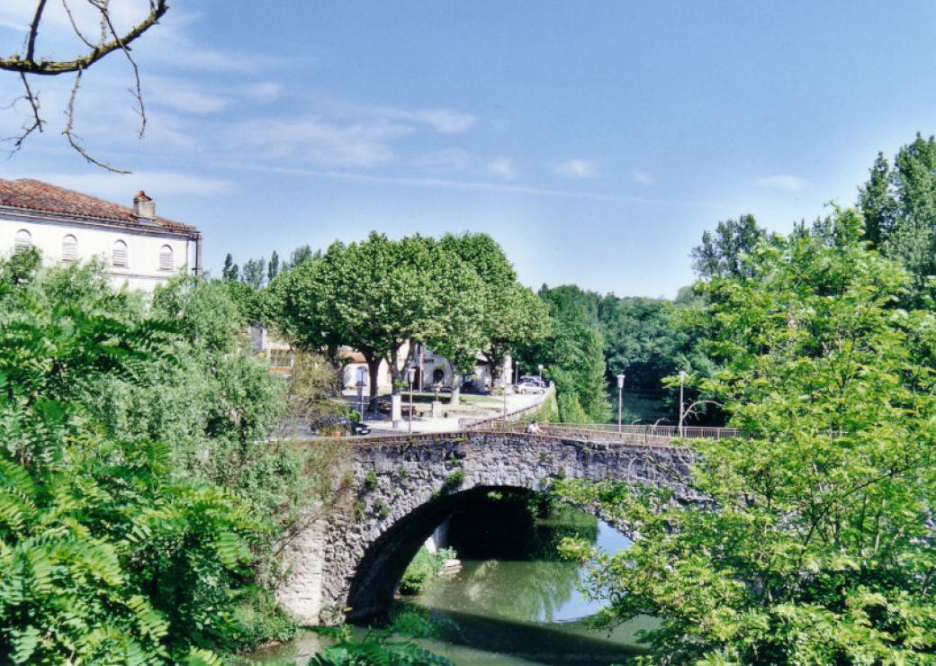 Pont ancien au dessus d'une rivière. Ciel bleu, paysage vert