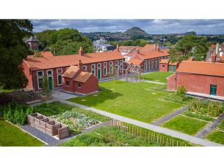 Vue aérienne d'un quartier urbain composé de bâtiments longs, hauts d'un seul étage, espacés par des carrés de pelouse. Au loin se dresse la silhouette d'un terril.