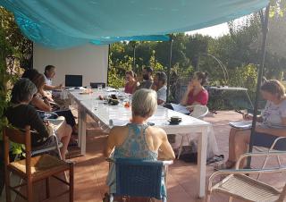 Protégés du soleil par un tissu bleu, une dizaine de personnes sont réunis autour d'une table dans un jardin